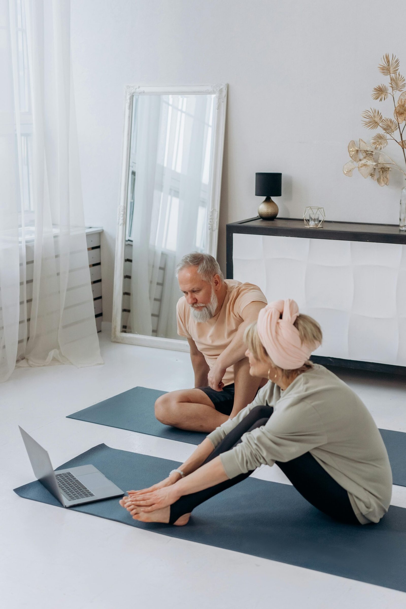 Senior couple doing yoga at home with a laptop guide, promoting a healthy lifestyle.